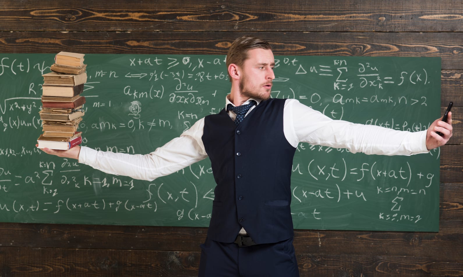 Teacher standing in front of a chalk board balancing books