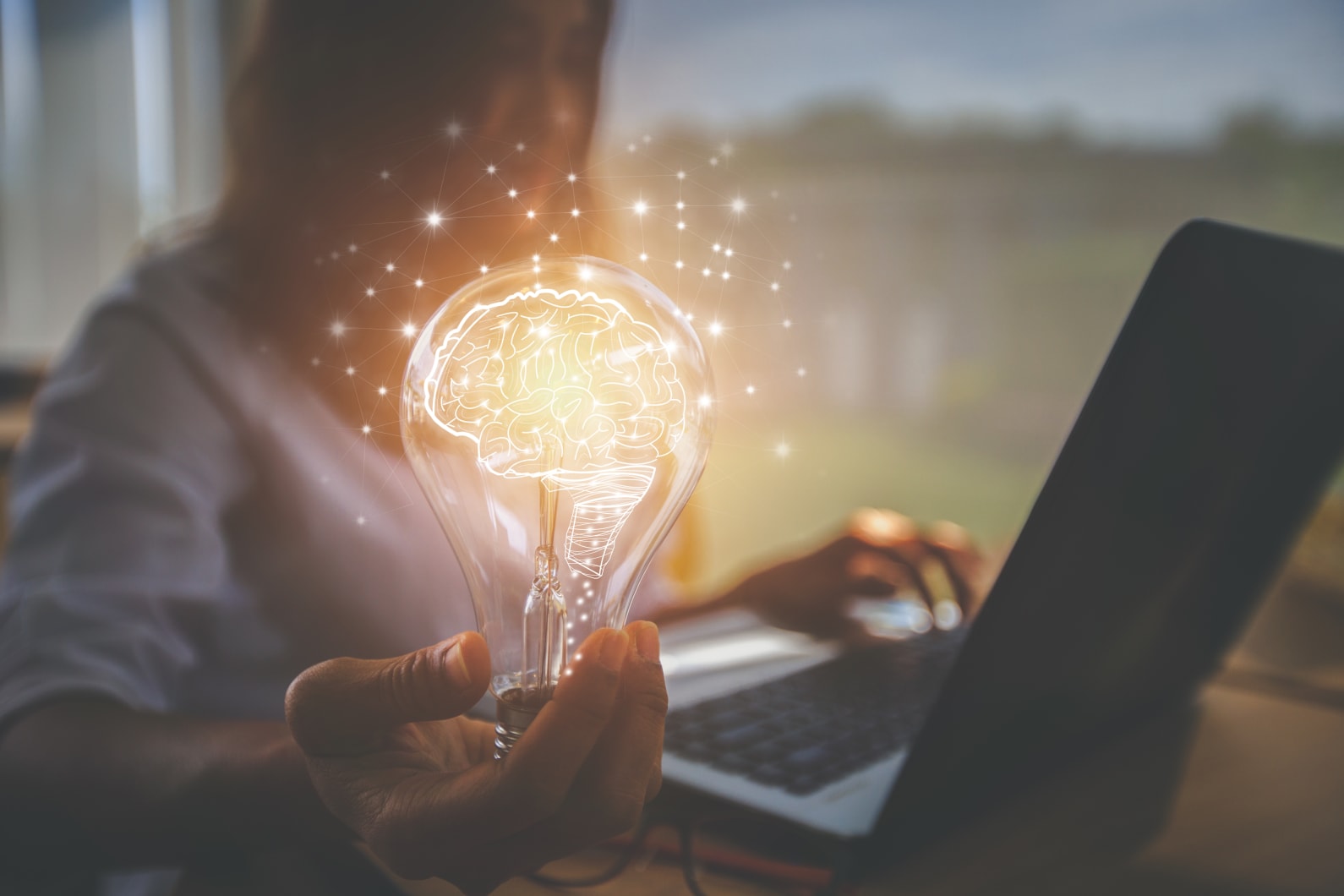 Person on laptop holding bright lightbulb