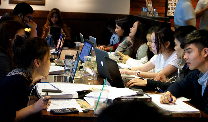 Students crammed at a table studying with their laptops and paperwork. 