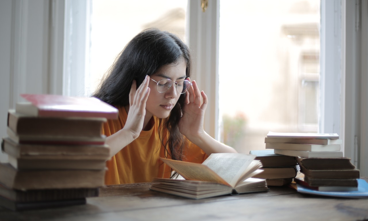 Women sitting at a desk reading with her hands pressed against her temples