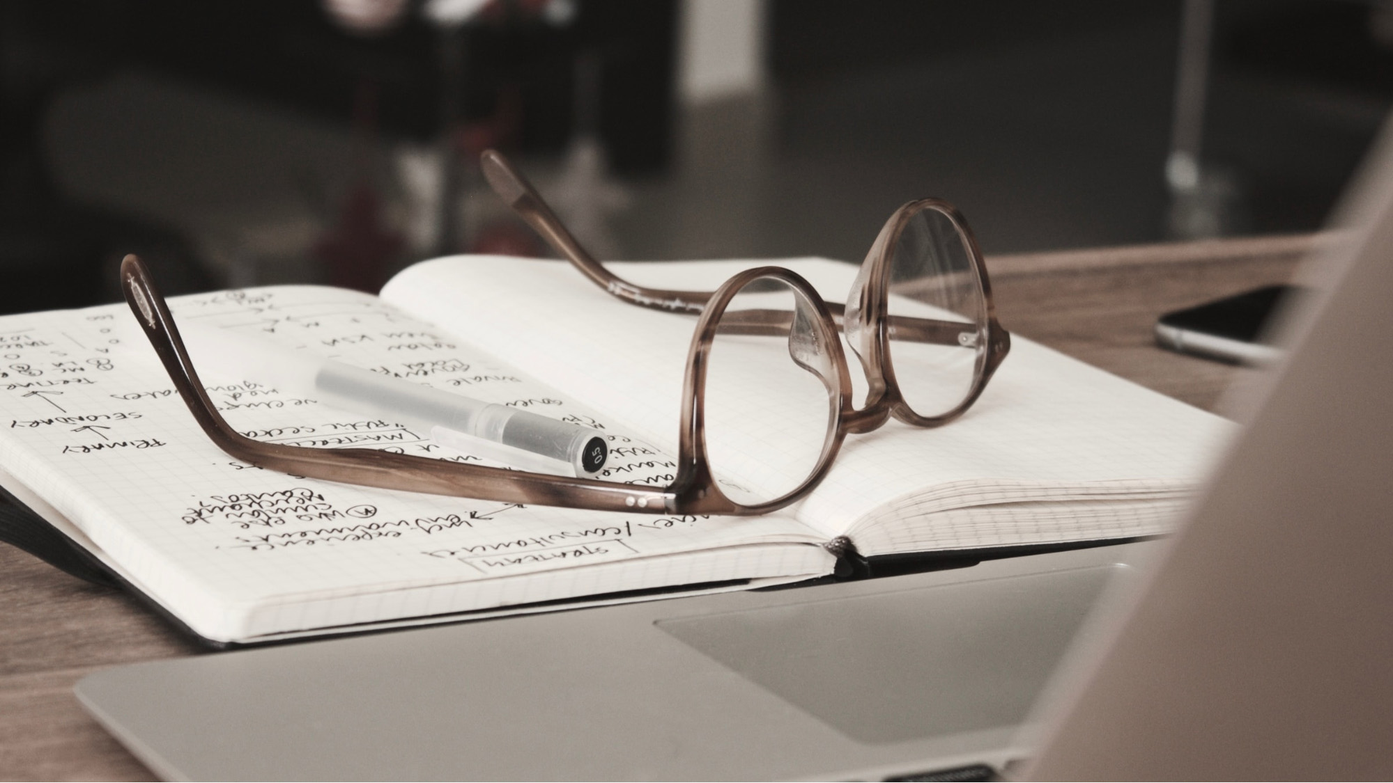 A laptop, notebook and glasses lying on a table