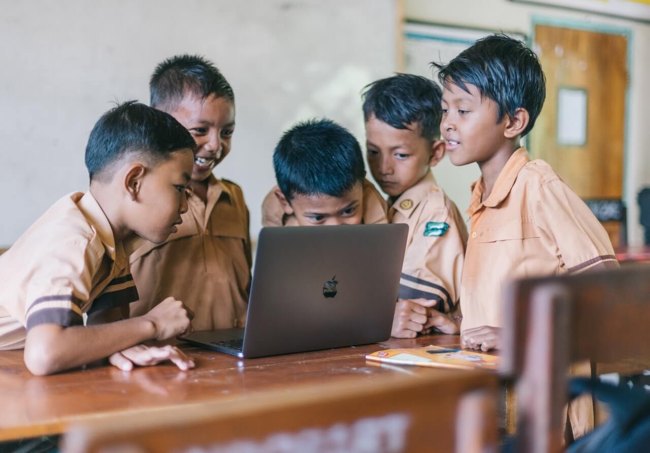 Young students gathered around a laptop in the classroom