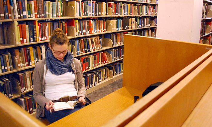 Student reading a book at a desk in a library.